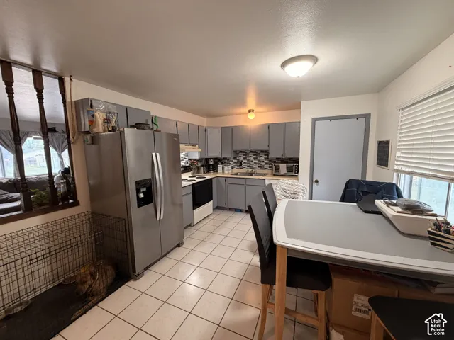 Kitchen featuring tile flooring, gray cabinetry, stainless steel refrigerator, and a tiled backsplash