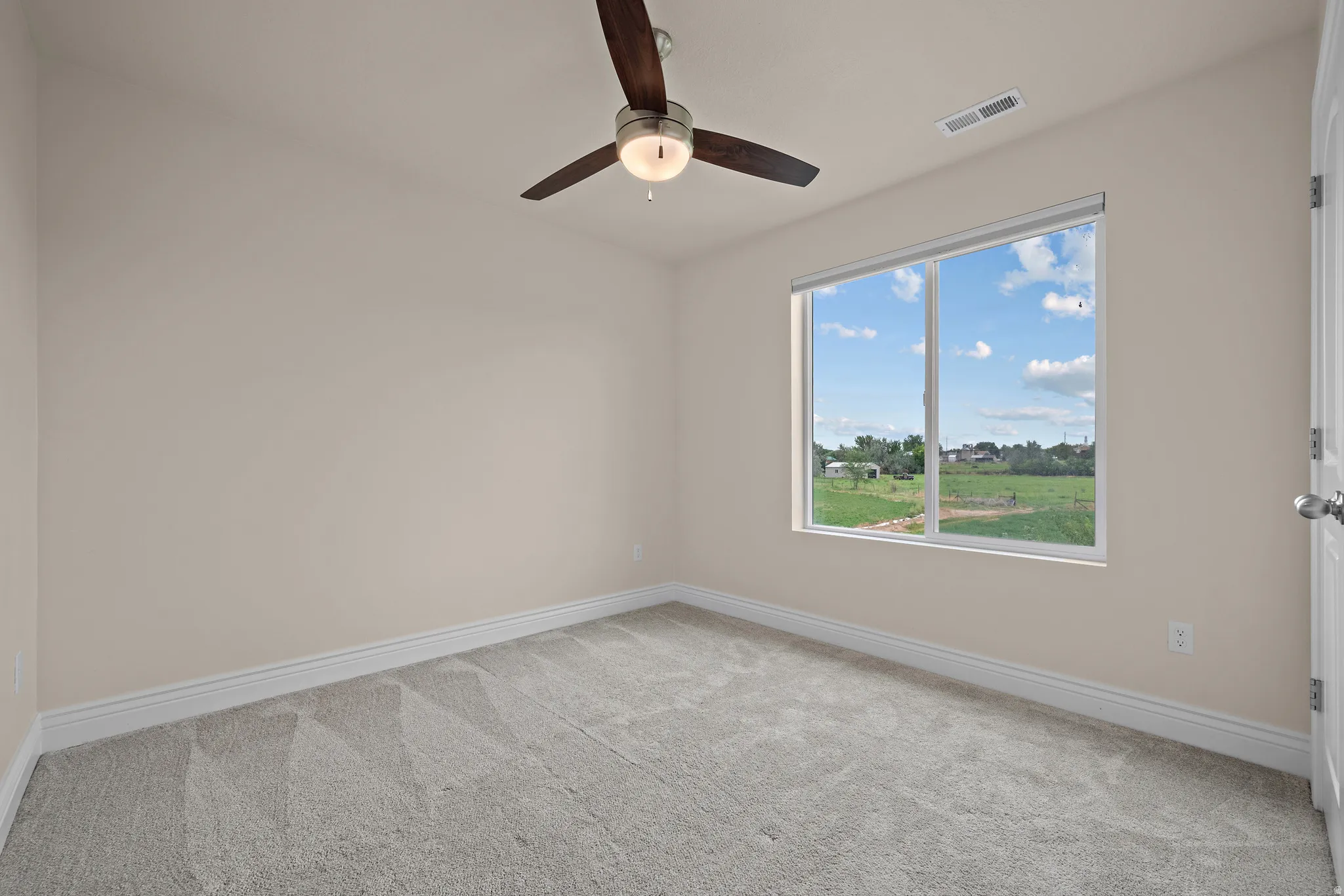 Neutral toned walls, light gray carpeting, ceiling fan with integrated lighting, and a large window