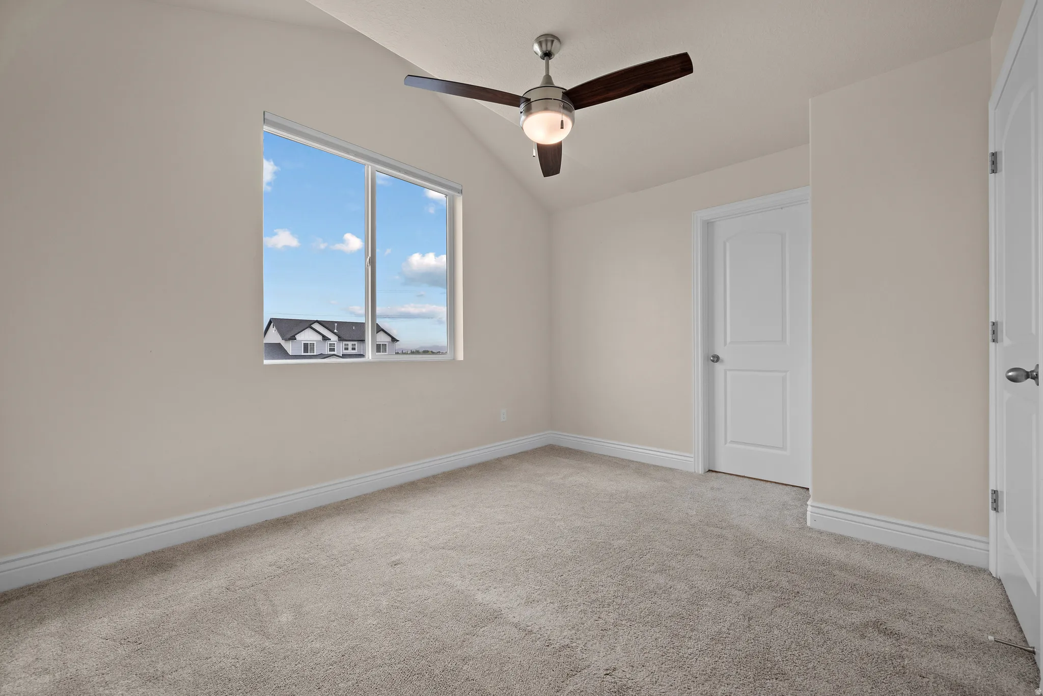 Vaulted ceiling with a ceiling fan, carpeted flooring, and a large window