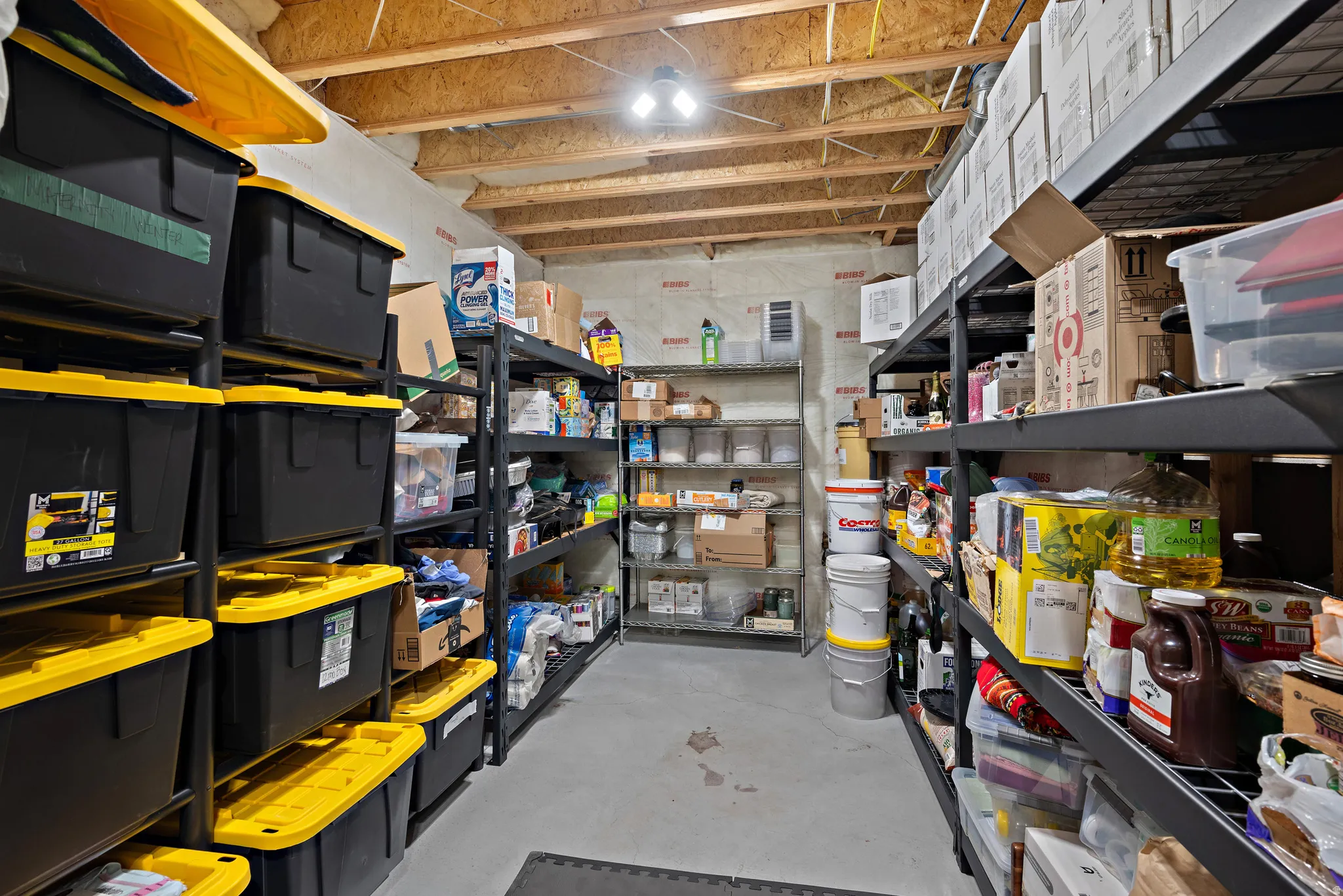 Unfinished basement space with exposed ceiling joists and concrete flooring, featuring multiple shelving units
