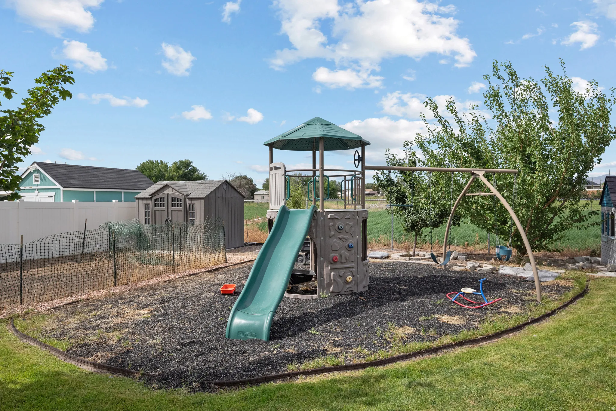 Expansive backyard featuring a fenced garden area, a storage shed, and a dedicated play area with a swing set and slide structure