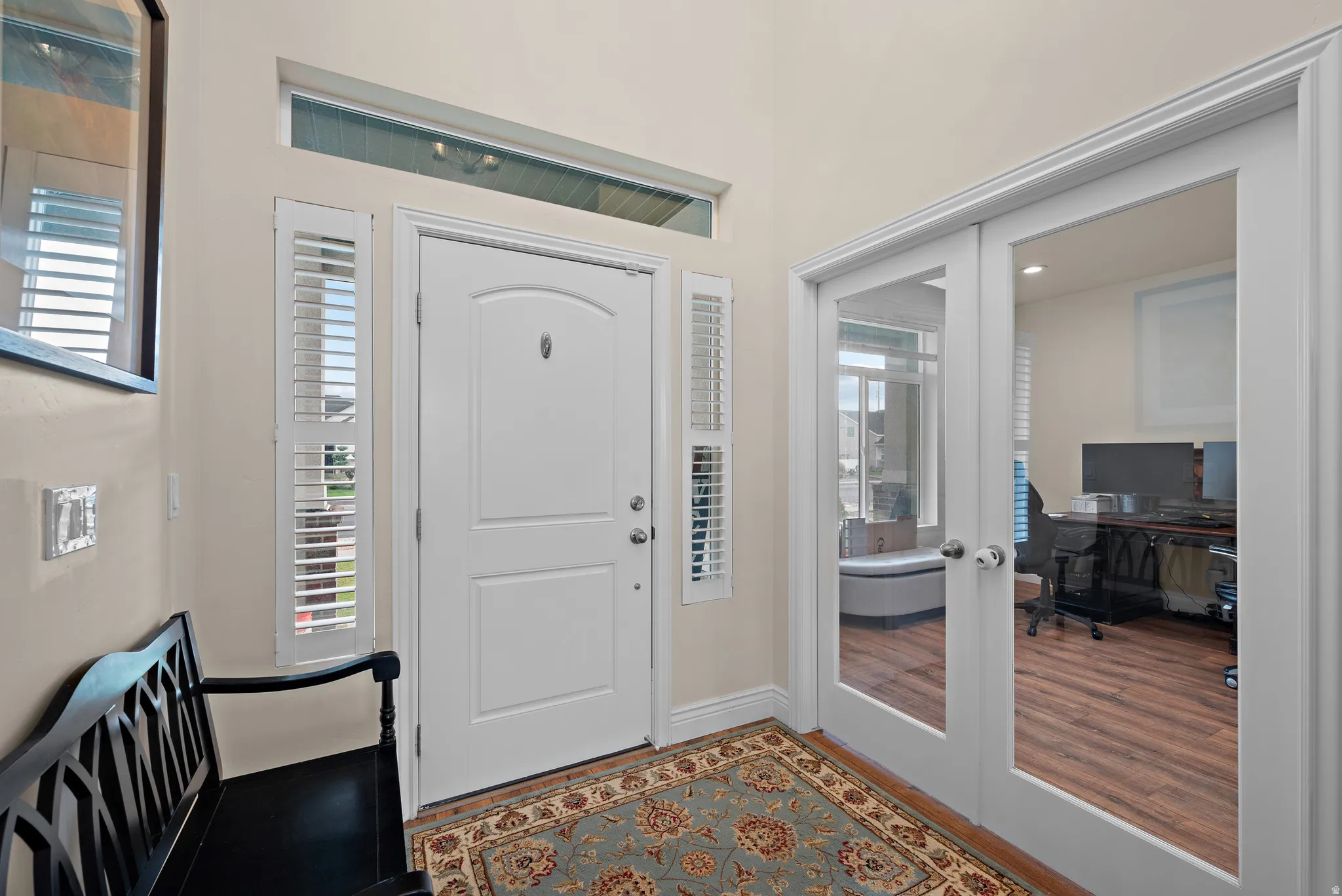 Entryway with a white paneled door, transom window, and sidelights with plantation shutters
