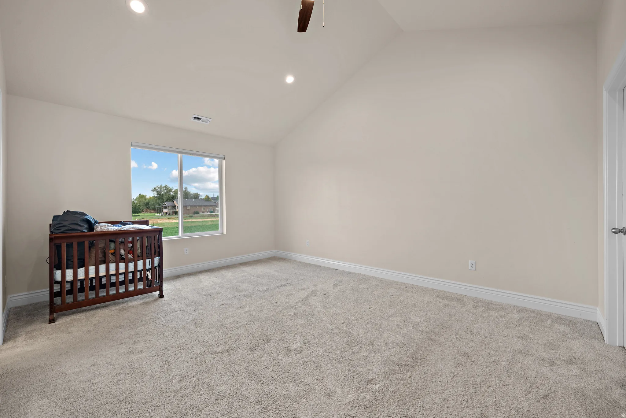 Vaulted ceiling, recessed lighting, ceiling fan, neutral carpet, and white trim