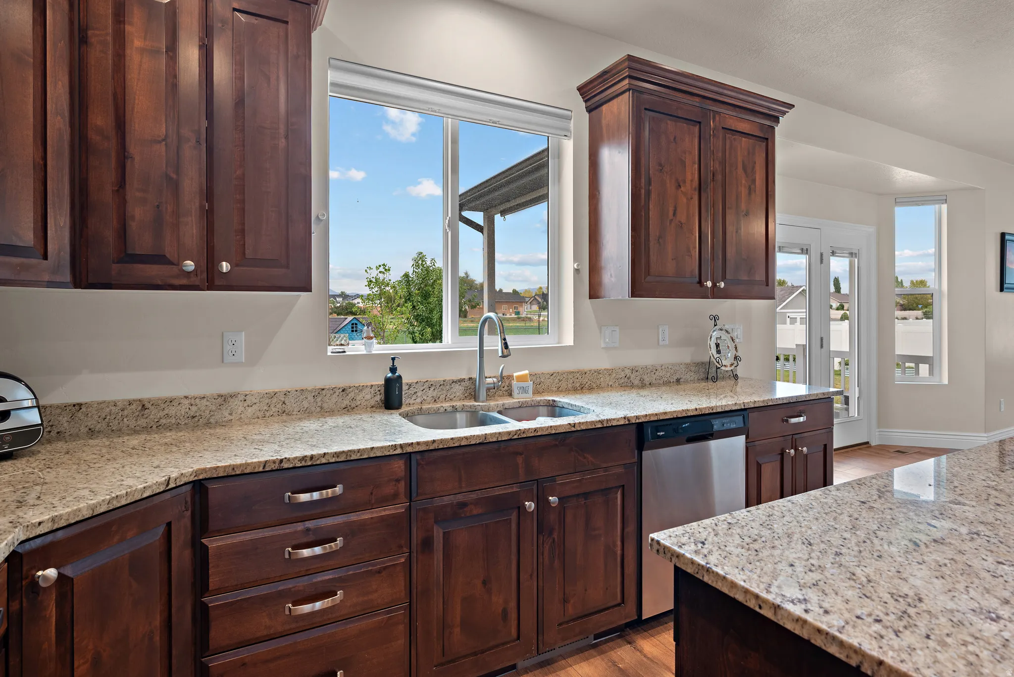 Rich wood cabinetry with crown molding, stone countertops, stainless steel undermount sink, and a stainless steel dishwasher