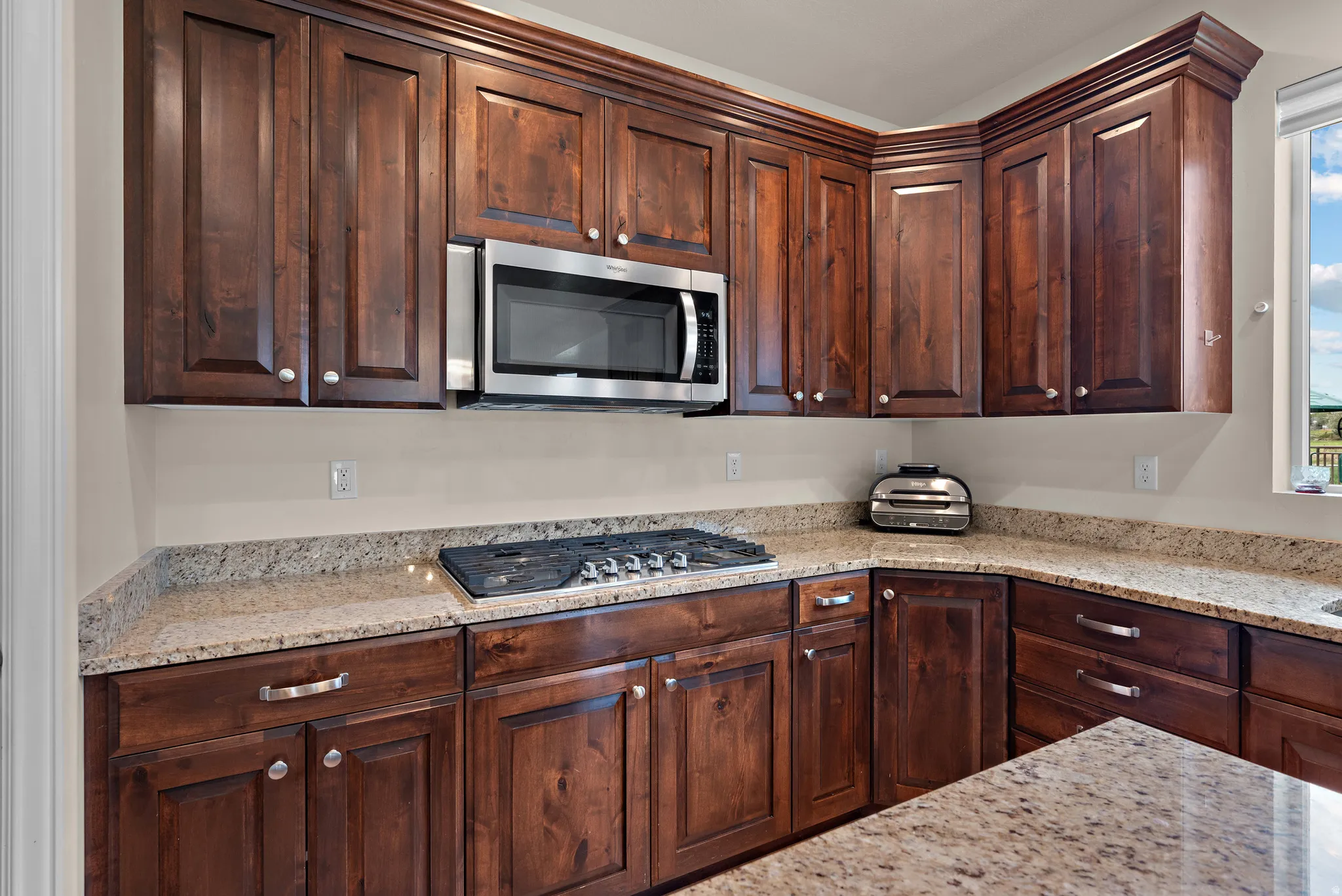 Wood cabinetry with crown molding, granite countertops, built-in stainless steel microwave, and gas cooktop