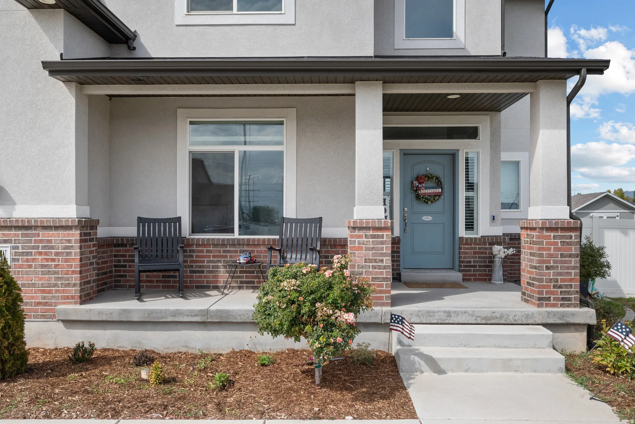 Covered porch with brick and stucco detailing, a paneled entry door, and a concrete walkway