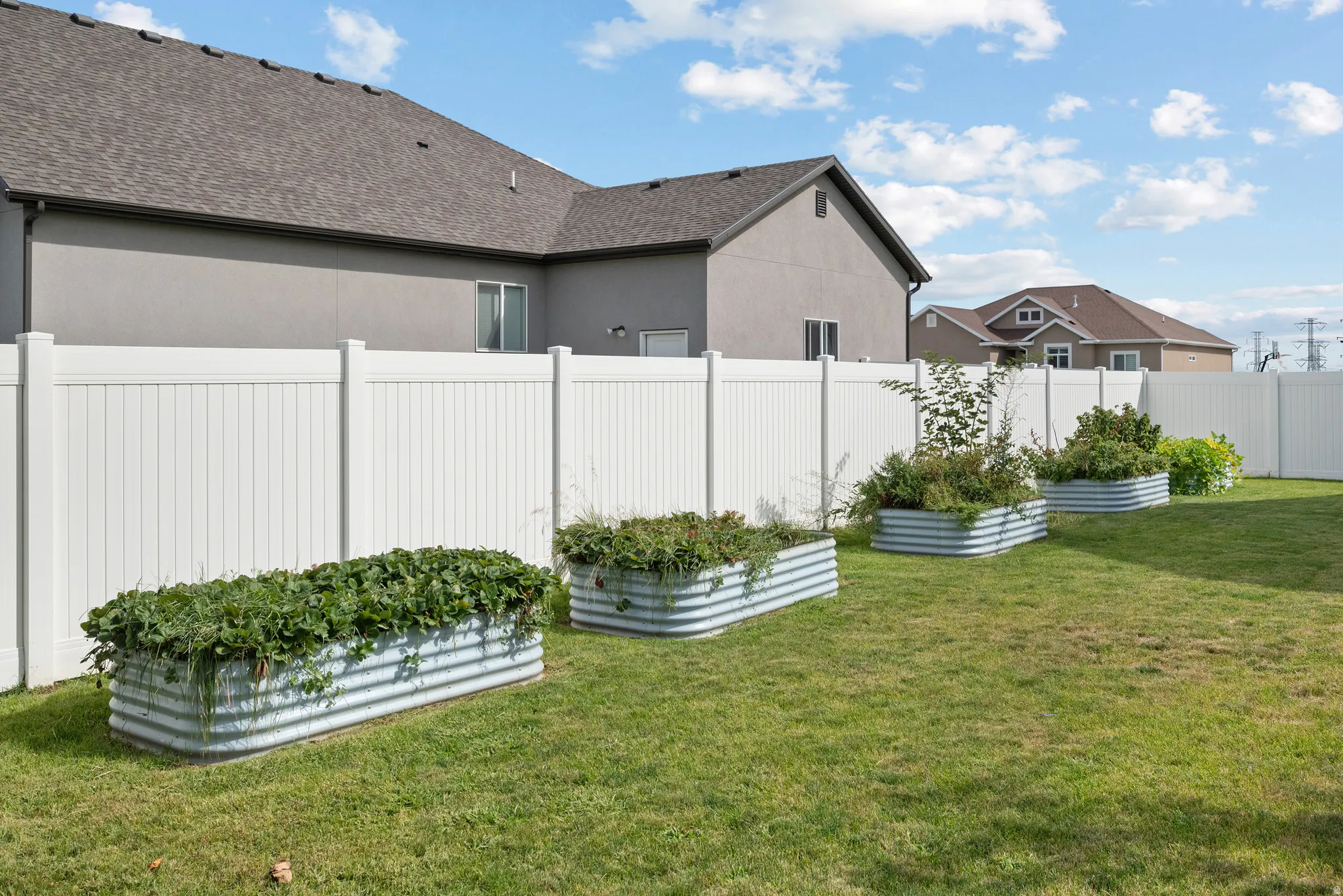 Private backyard featuring a white vinyl fence, established lawn, and multiple corrugated metal planter boxes
