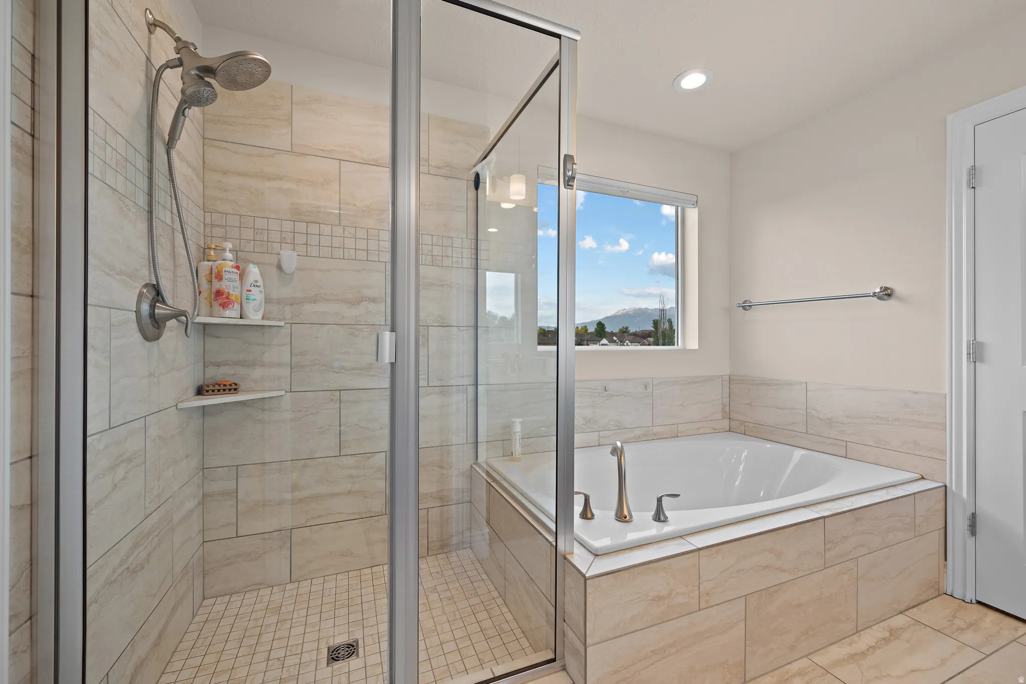 Walk-in shower with tile surround and glass enclosure, separate soaking tub with tile surround, and recessed lighting
