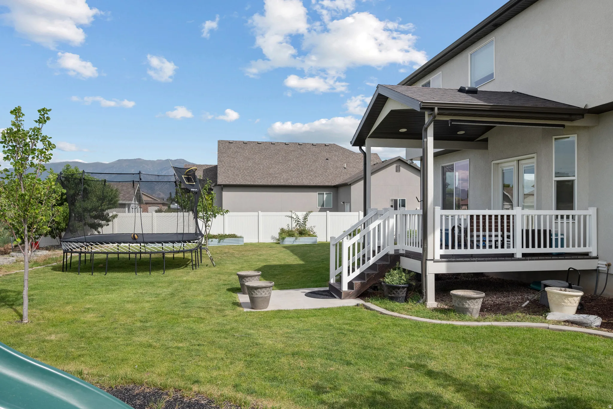 Expansive backyard featuring a covered patio, white railing, mature tree, and a mountain backdrop