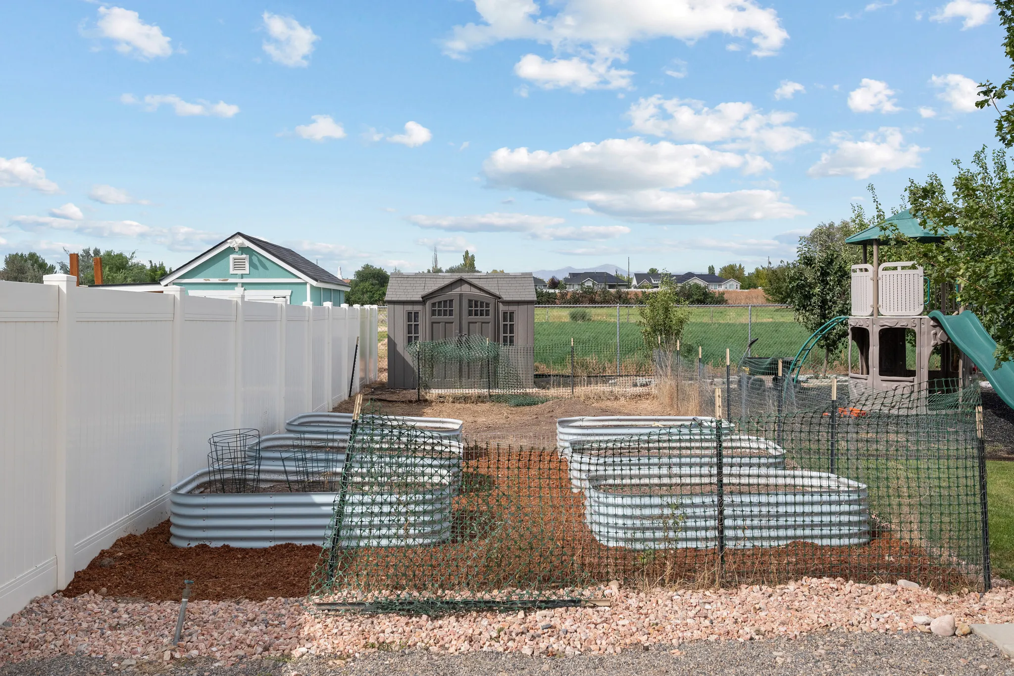 Private fenced yard with multiple raised garden beds, a storage shed, and a play structure