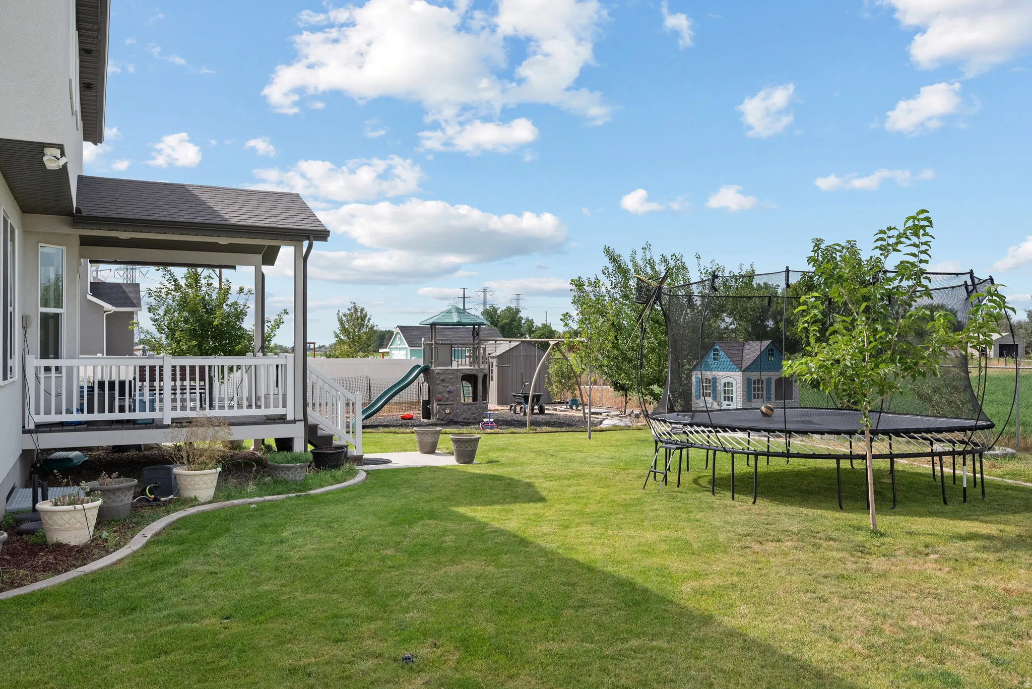 Expansive backyard featuring a covered patio, manicured lawn, paved walkway, and established trees