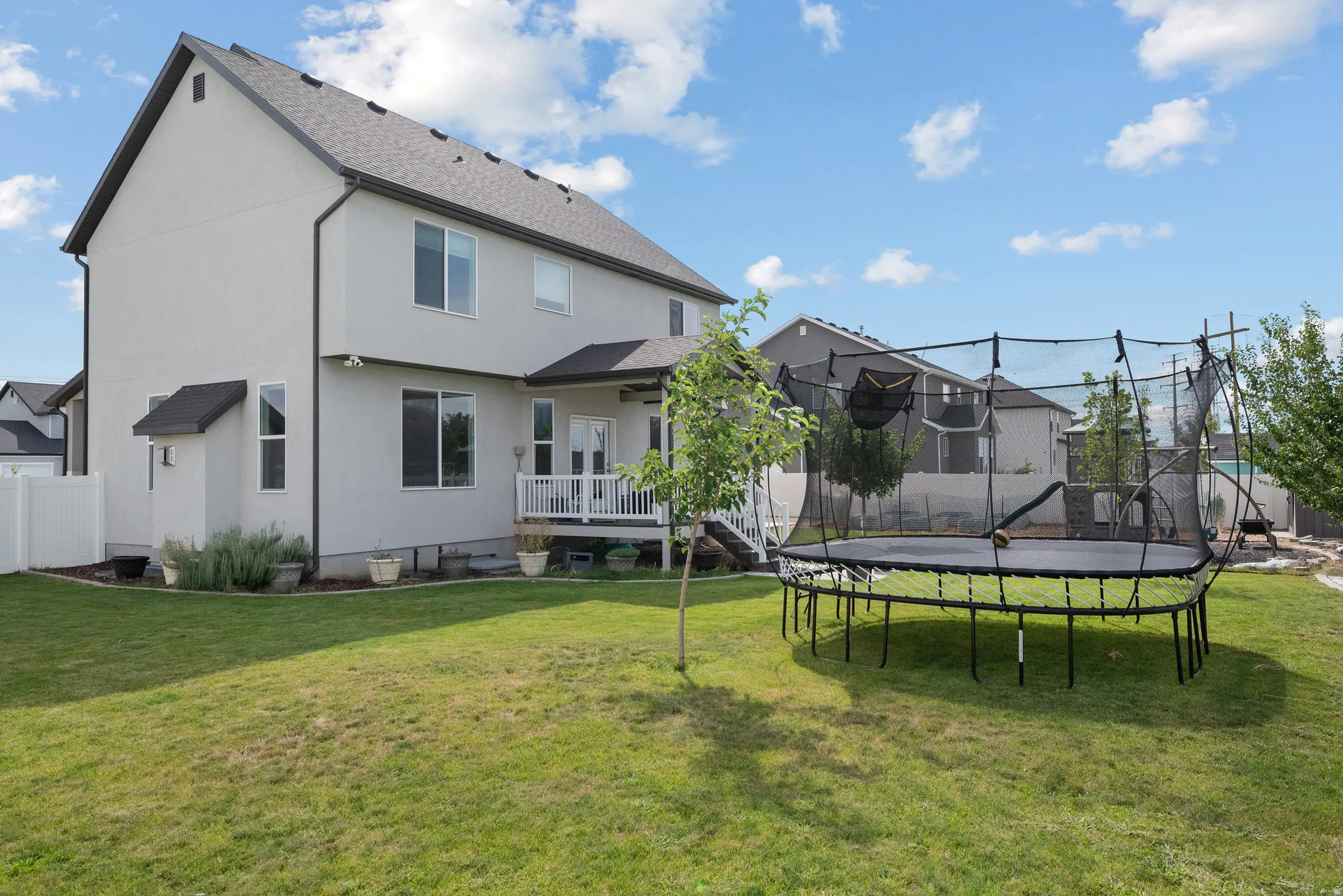 Stucco exterior with a pitched roof, rear deck with white railings, and a manicured lawn