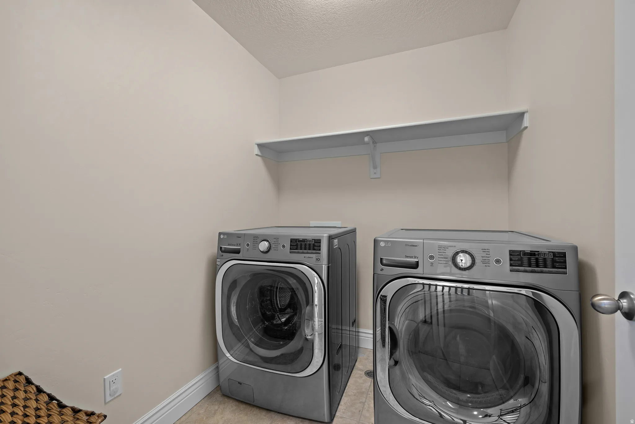 Laundry area with neutral wall tones, tile flooring, and a built-in wall shelf