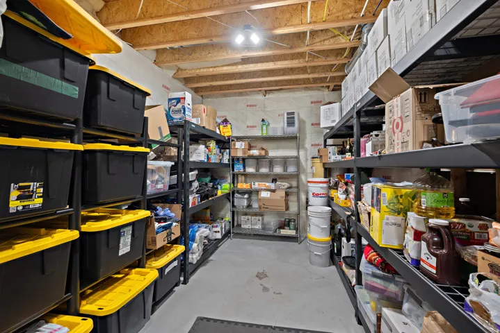 Unfinished basement space with exposed ceiling joists and concrete flooring, featuring multiple shelving units