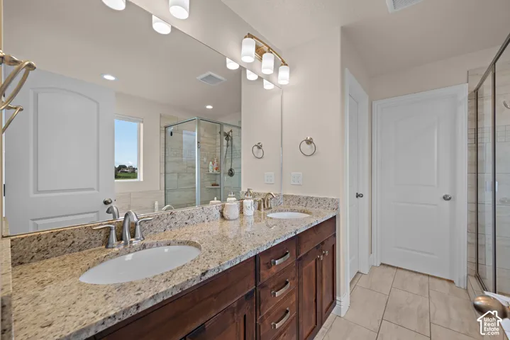 Dual undermount sinks with brushed nickel fixtures, granite countertops, wood-finish cabinetry, a glass-enclosed shower, and tile flooring