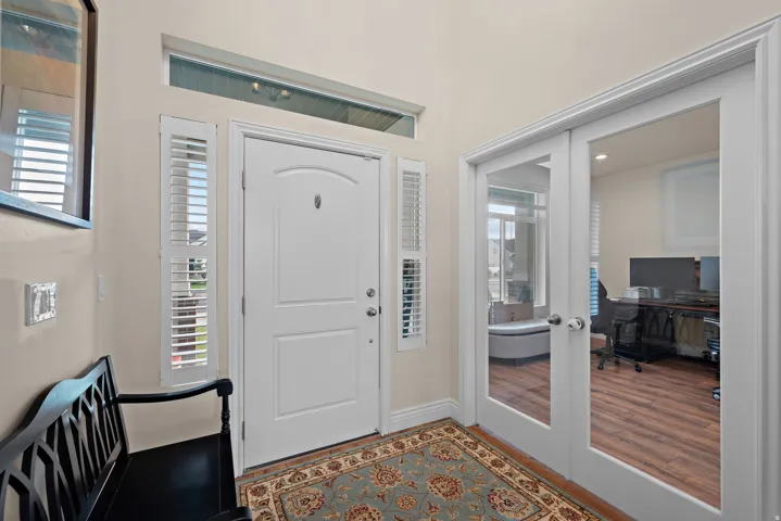 Entryway with a white paneled door, transom window, and sidelights with plantation shutters