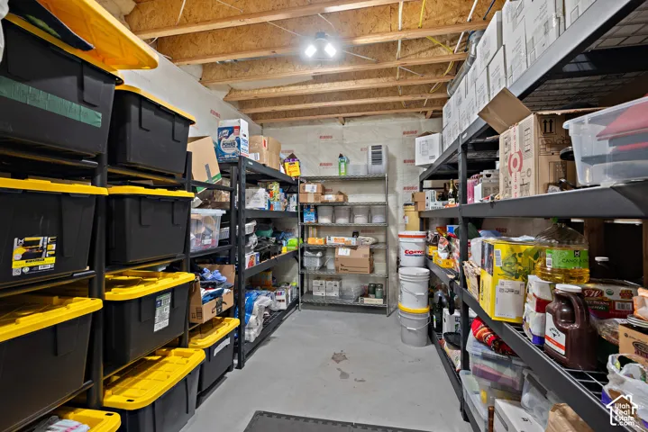 Unfinished basement space with exposed ceiling joists and concrete flooring, featuring multiple shelving units