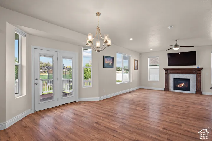 Wood-finish flooring throughout, French doors with direct outdoor access, a tiled fireplace with a substantial wood mantel, multiple windows for natural illumination, and a ceiling fan