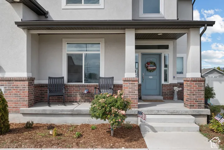 Covered porch with brick and stucco detailing, a paneled entry door, and a concrete walkway