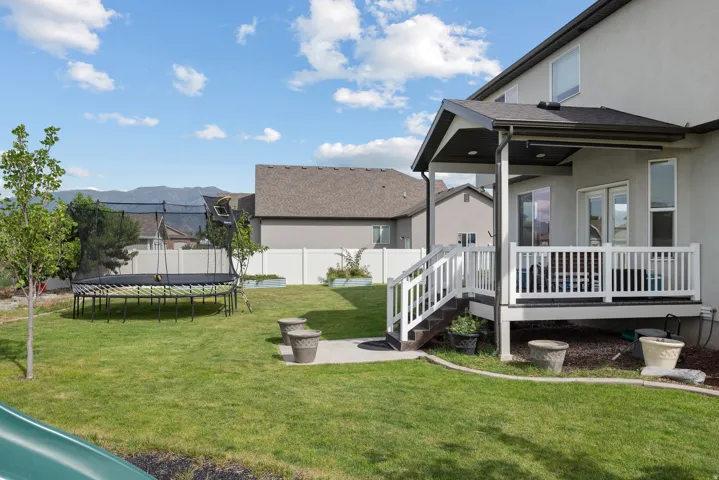 Expansive backyard featuring a covered patio, white railing, mature tree, and a mountain backdrop