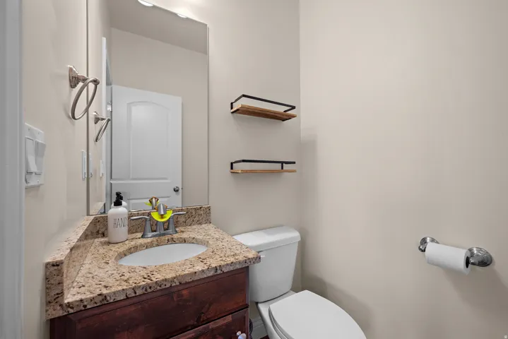 Wood-finish vanity with an undermount sink, granite countertop, wall-mounted mirror, and overhead vanity lighting