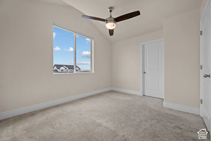 Vaulted ceiling with a ceiling fan, carpeted flooring, and a large window