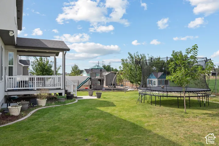 Expansive backyard featuring a covered patio, manicured lawn, paved walkway, and established trees