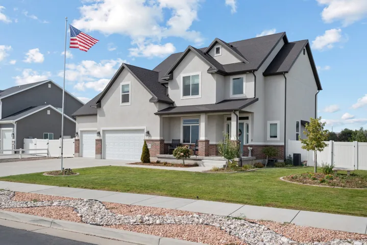 Contemporary two-story residence with stucco and brick accents, featuring a covered front porch, a two-car garage, and a fenced backyard