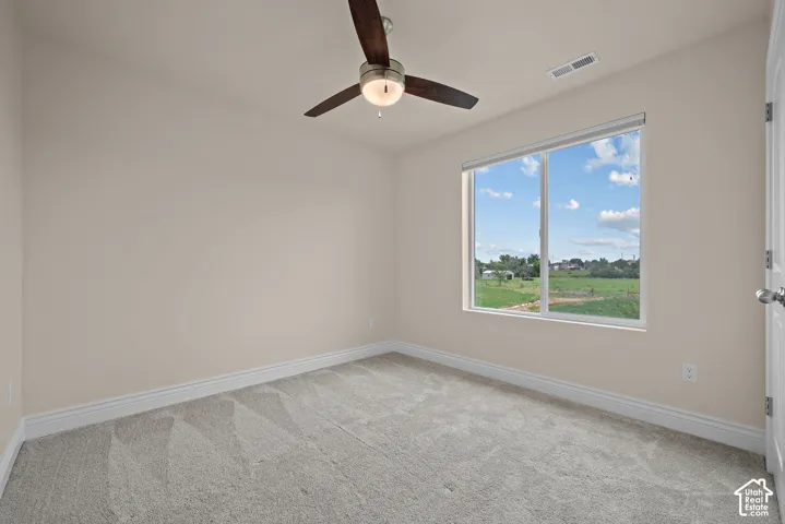 Neutral toned walls, light gray carpeting, ceiling fan with integrated lighting, and a large window