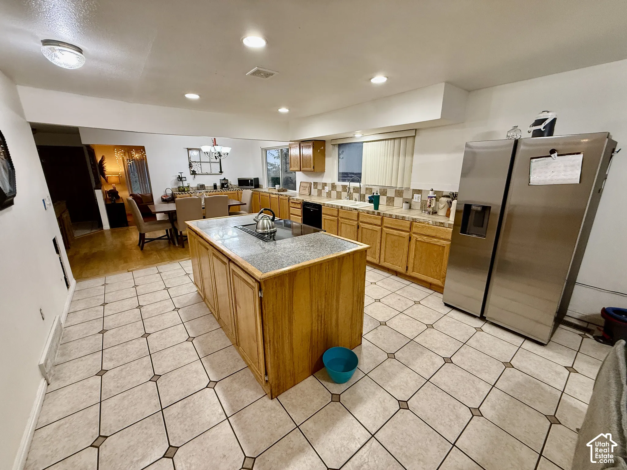 Spacious kitchen featuring an island with a built-in cooktop, light wood cabinetry, stainless steel appliances, tile flooring, and recessed lighting