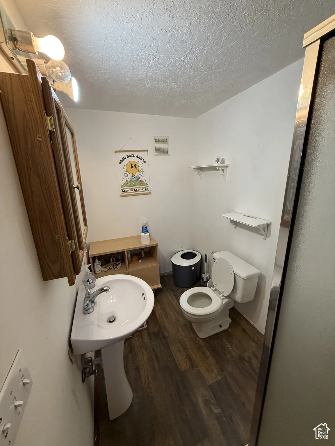 Pedestal sink with chrome faucet, wood-finish flooring, and wall-mounted vanity mirror with integrated lighting