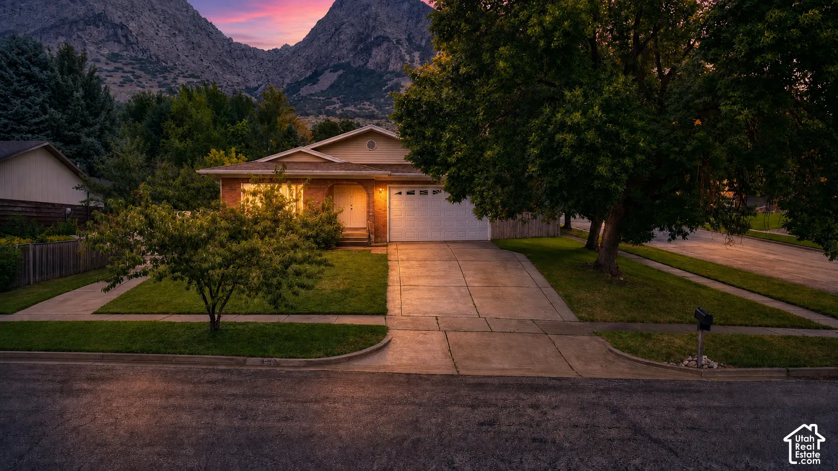 Brick exterior with an attached garage, paved driveway, and established landscaping