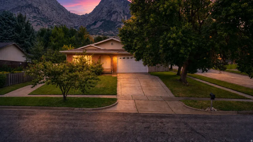 Brick exterior with an attached garage, paved driveway, and established landscaping