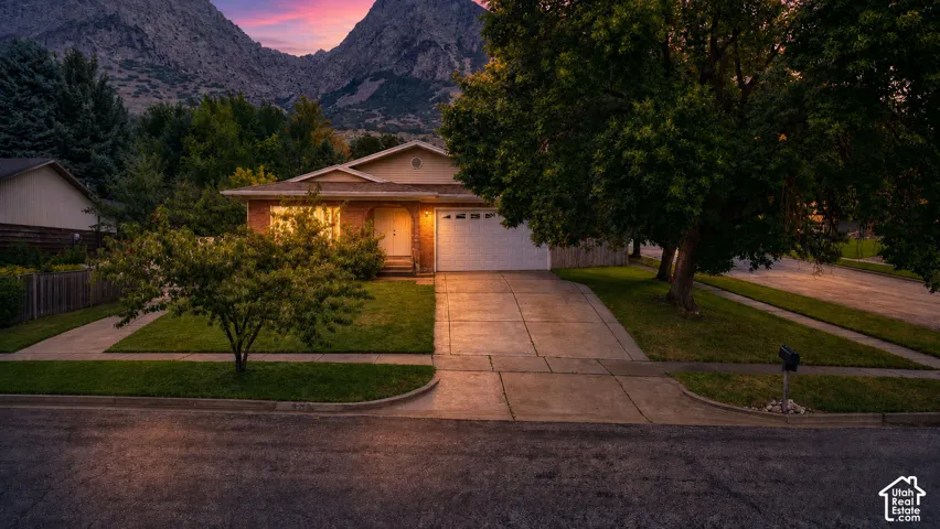 Brick exterior with an attached garage, paved driveway, and established landscaping
