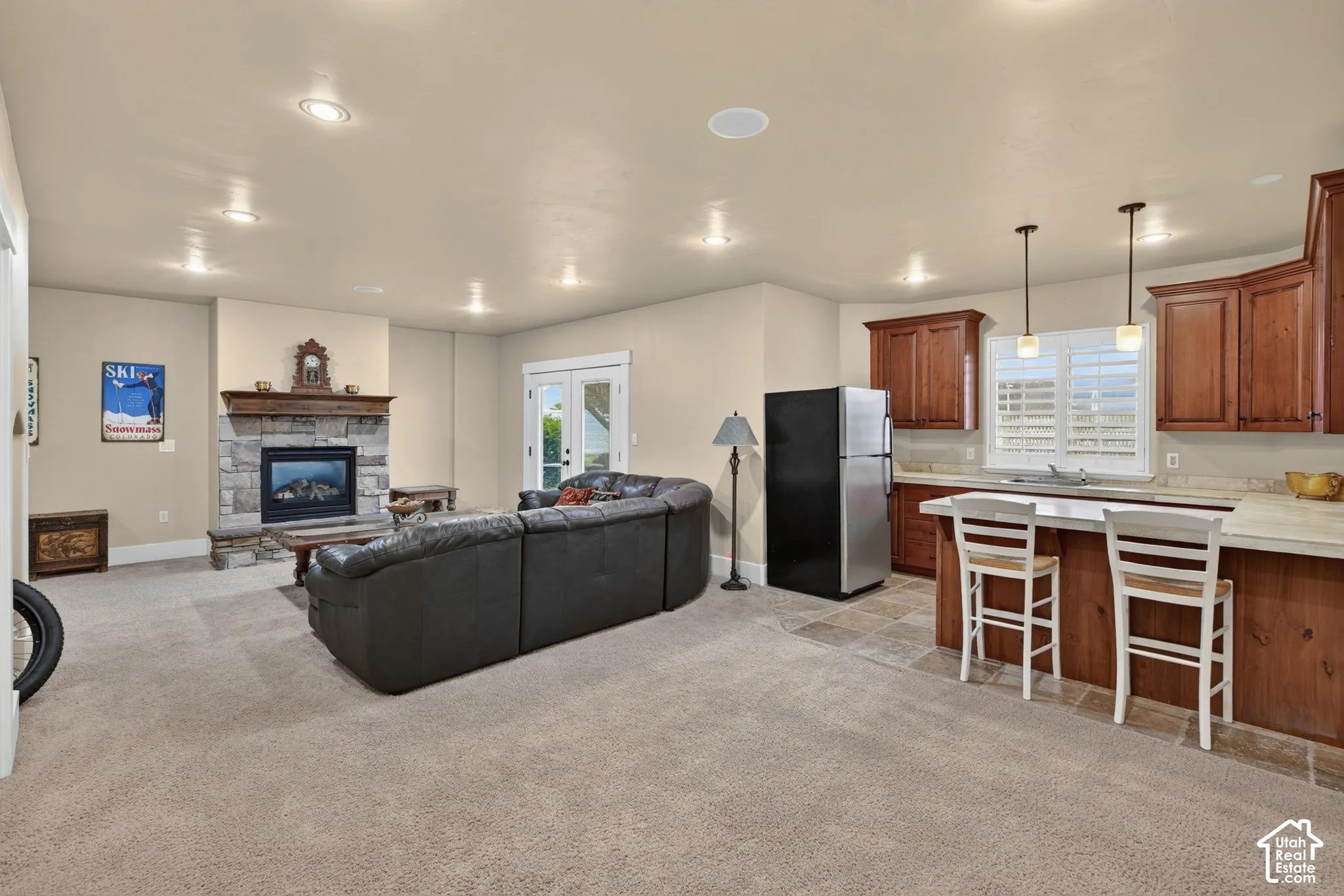 Recessed lighting, stone-clad fireplace, French doors, wood-finish cabinetry, and a built-in kitchen island