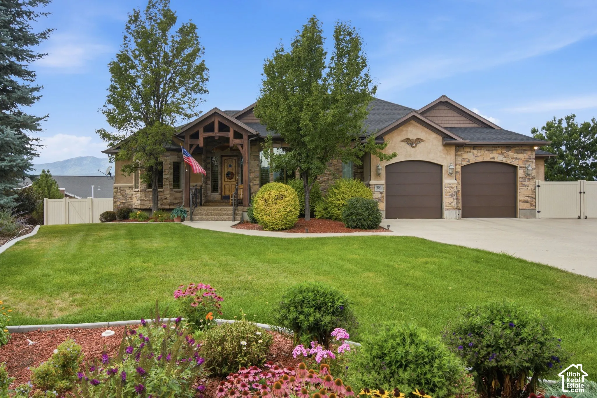 Stone facade home featuring a prominent front entrance, two-car garage with arched doors, mature landscaping, and a paved driveway