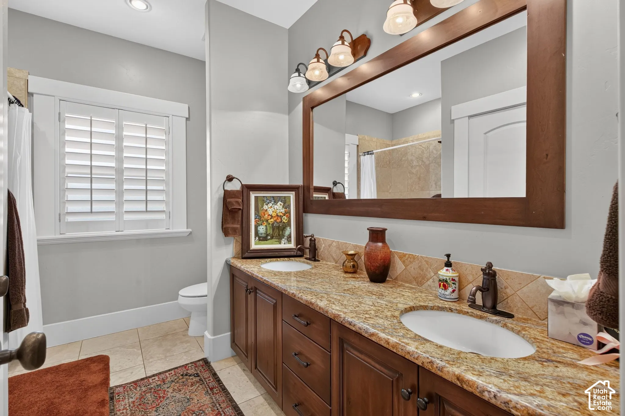 Dual vanity with granite countertop, integrated sinks, wood-finish cabinetry, and framed mirror