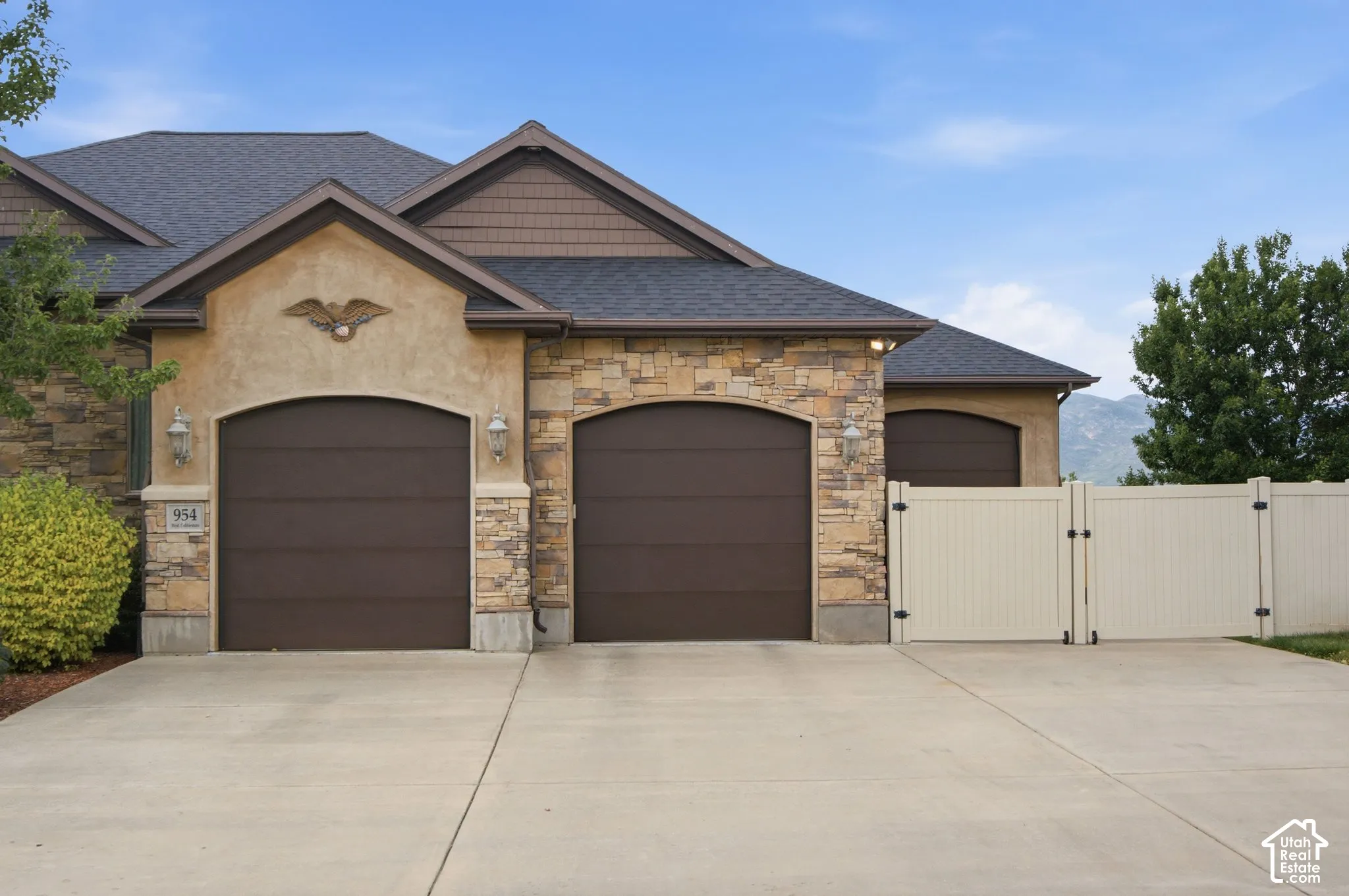 Stucco and stone exterior with arched garage doors, a multi-paneled privacy fence, and a concrete driveway