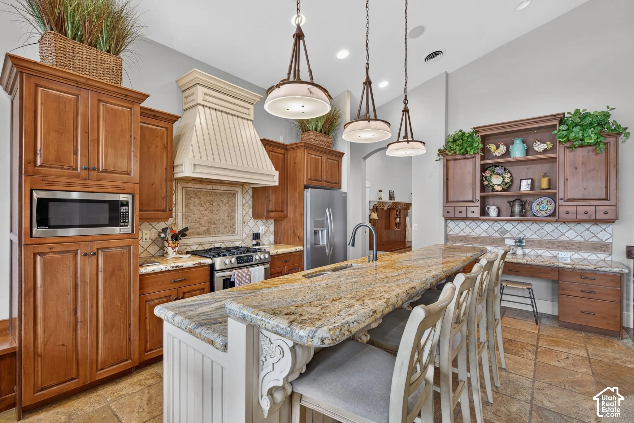 Spacious kitchen featuring extensive wood cabinetry, a large kitchen island with a stone-finish countertop, stainless steel appliances, and tile flooring