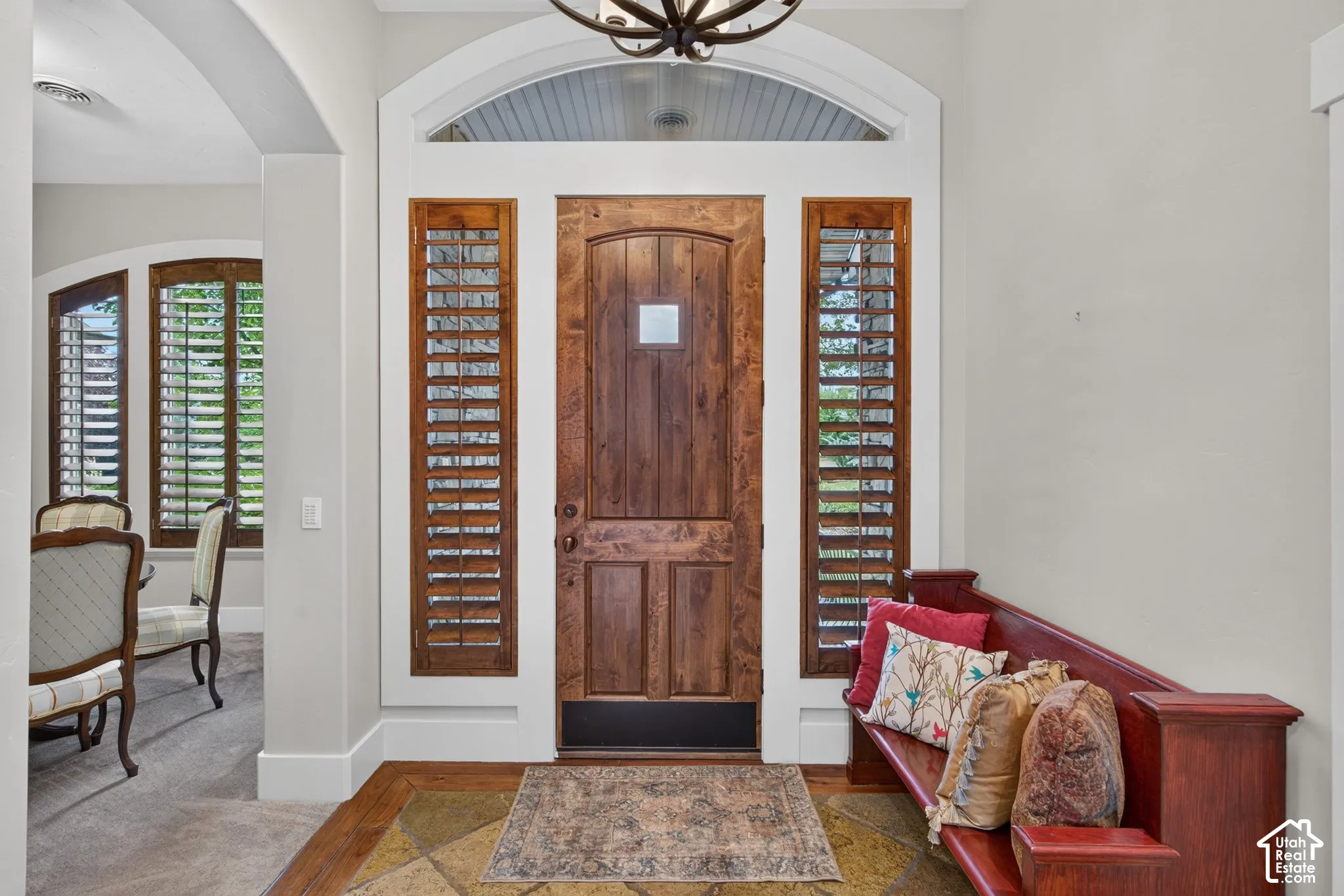 Arched transom window, wood-paneled entry door, sidelight windows with wood shutters, decorative overhead light fixture, and tile flooring with a wood border