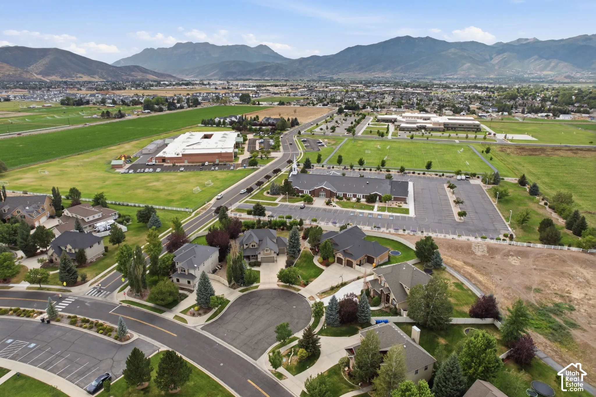 Residential neighborhood with mature landscaping, surrounded by open green spaces and distant mountains