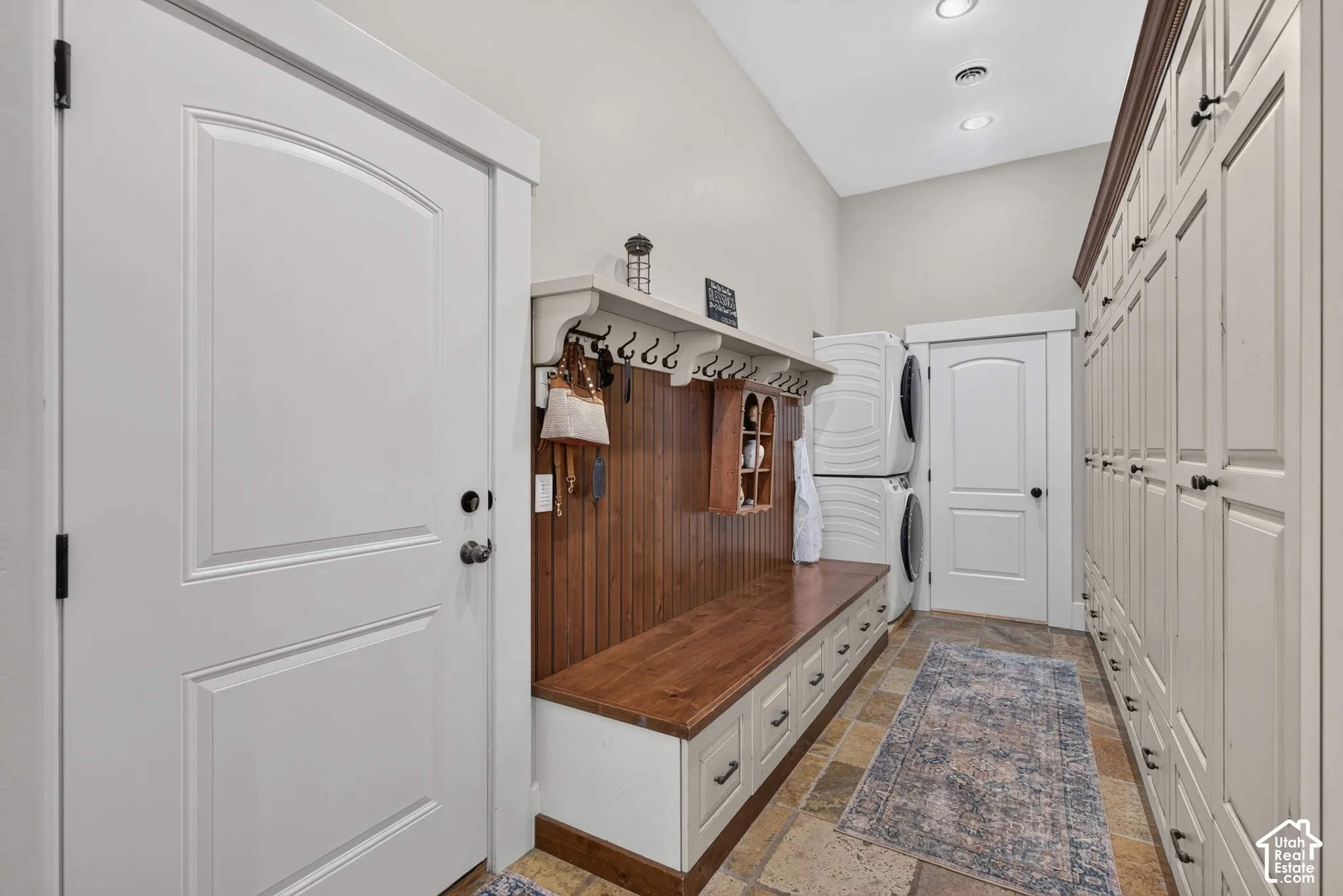 Built-in mudroom bench with storage, floor-to-ceiling cabinetry, recessed lighting, and stone tile flooring