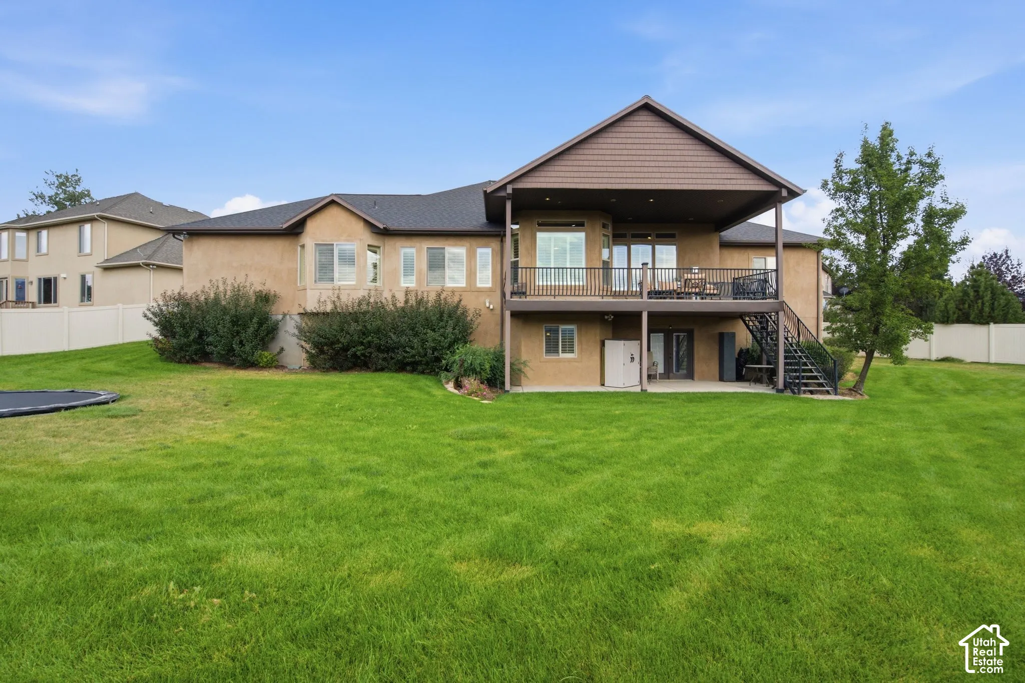 Expansive green lawn, stucco exterior, upper-level deck, covered lower patio, and mature landscaping