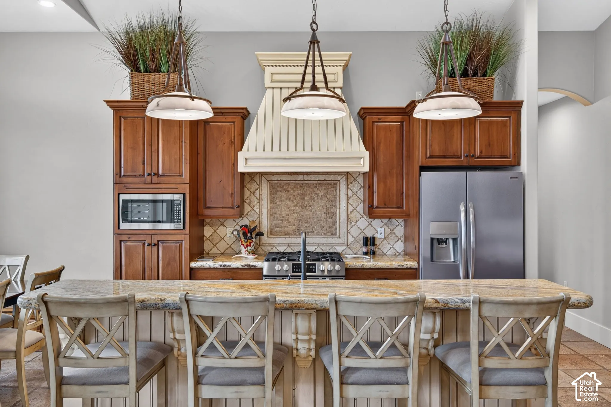 Kitchen island with a granite countertop, gas cooktop, built-in microwave, and stainless steel refrigerator
