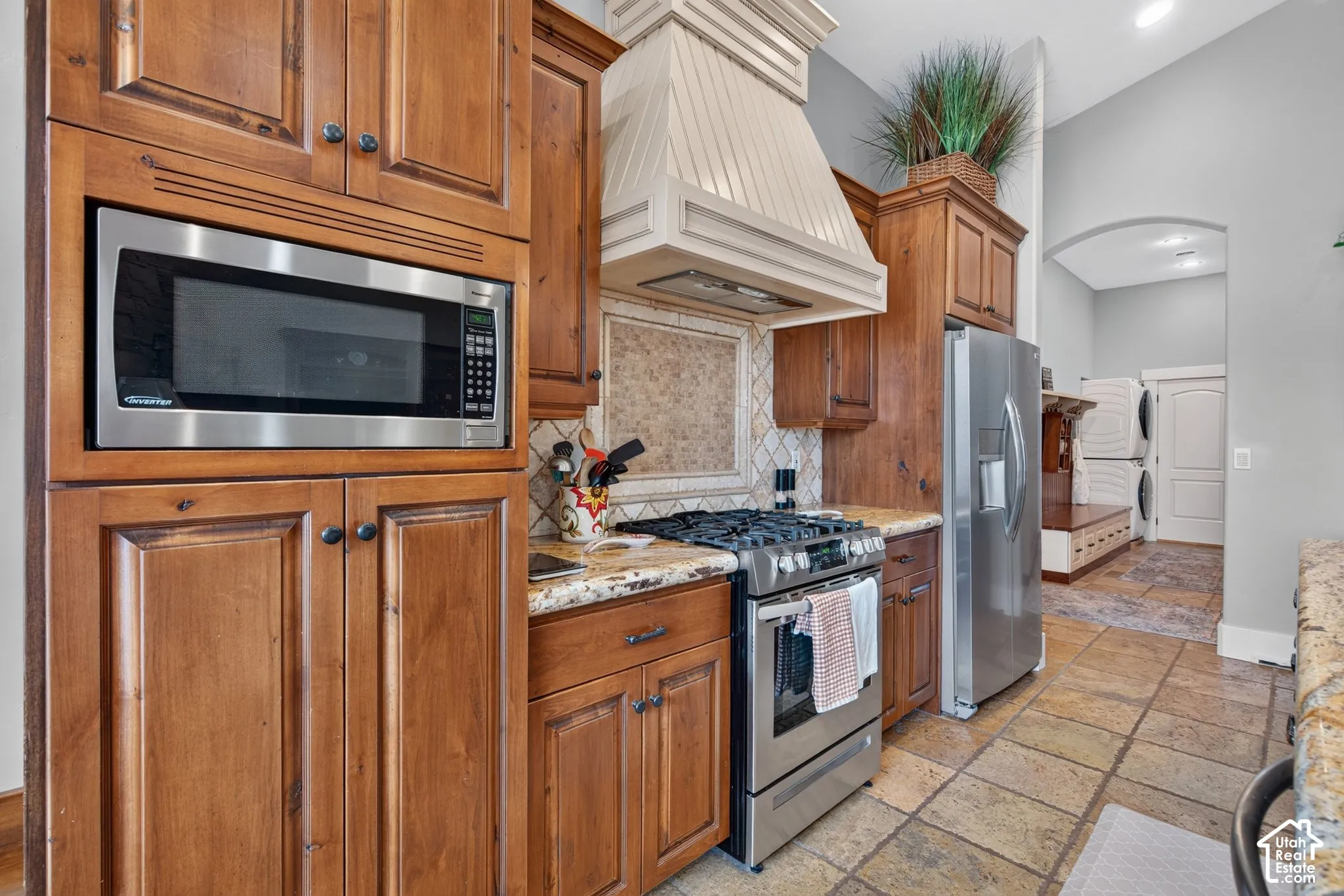 Kitchen featuring wood cabinetry, stainless steel appliances, stone countertops, a tile backsplash, and tile flooring