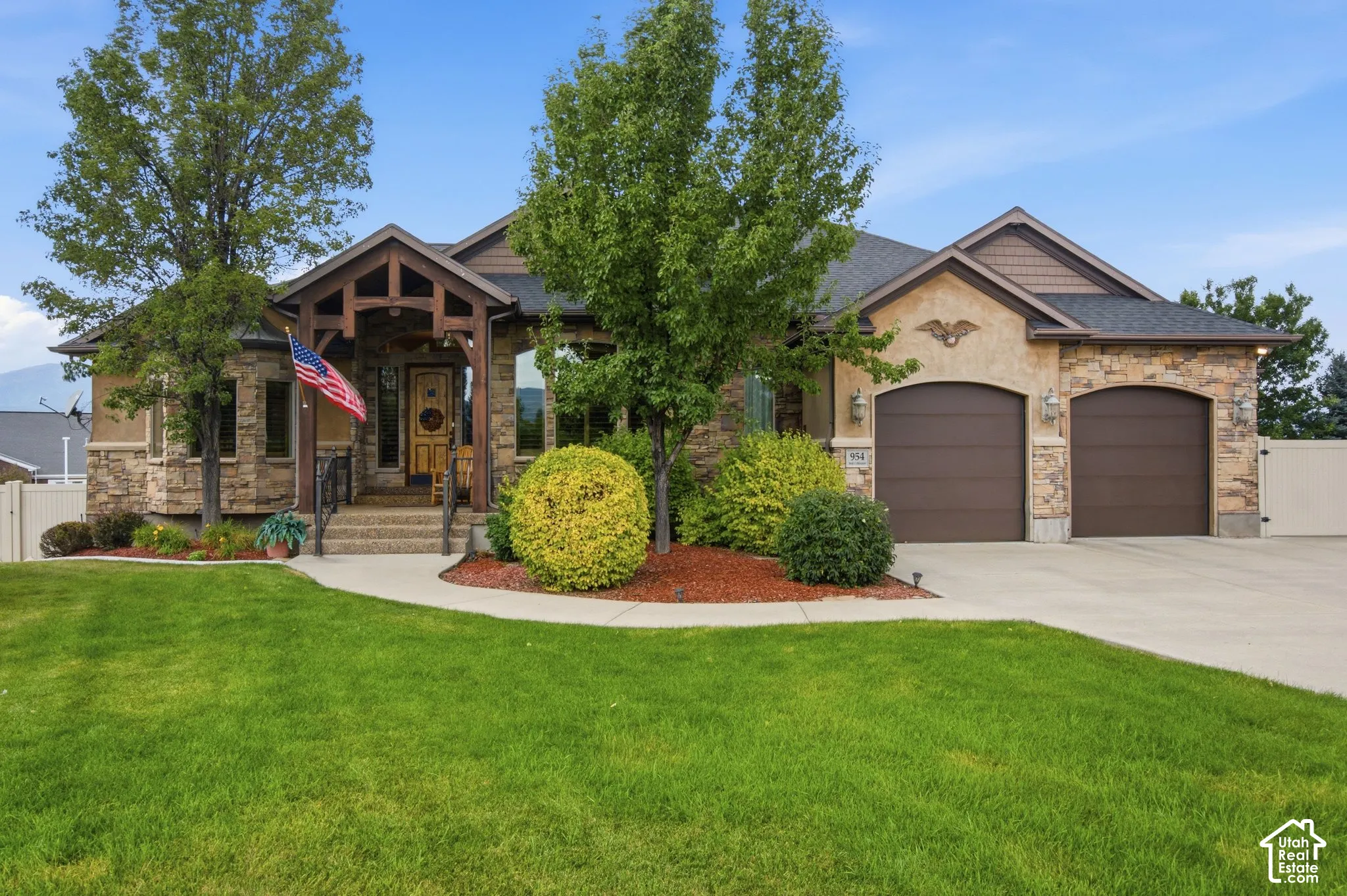 Stone and stucco exterior with a covered entry, dark wood-finish garage doors, and mature landscaping