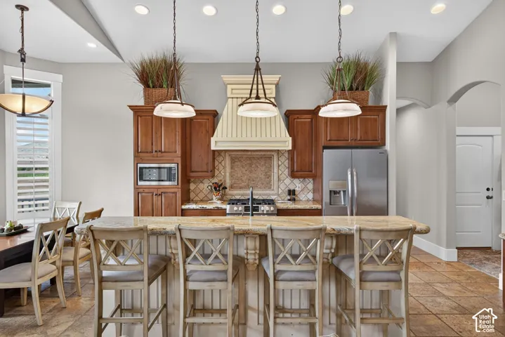 Gourmet kitchen featuring a large central island, stainless steel appliances, wood cabinetry, tile backsplash, and recessed lighting
