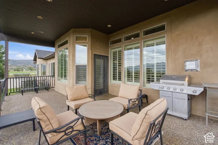 Covered patio with recessed lighting, stucco exterior, multiple large windows with plantation shutters, black wrought iron railing, and a built-in outdoor grill station