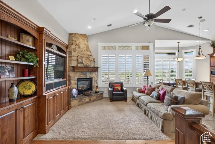 Built-in custom cabinetry, stone fireplace, vaulted ceiling, large windows with plantation shutters, and ceiling fan with integrated lighting