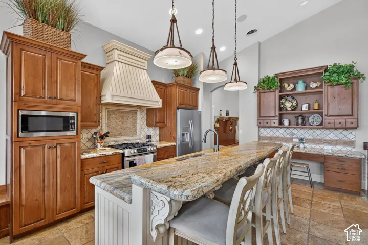 Spacious kitchen featuring extensive wood cabinetry, a large kitchen island with a stone-finish countertop, stainless steel appliances, and tile flooring